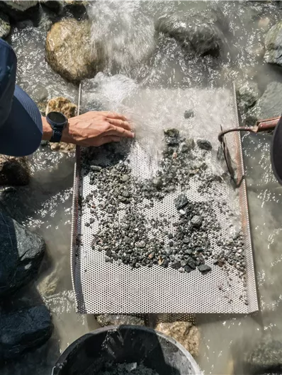 Two people are searching for rocks in the water. They are using a sieve to examine small stones and minerals.
