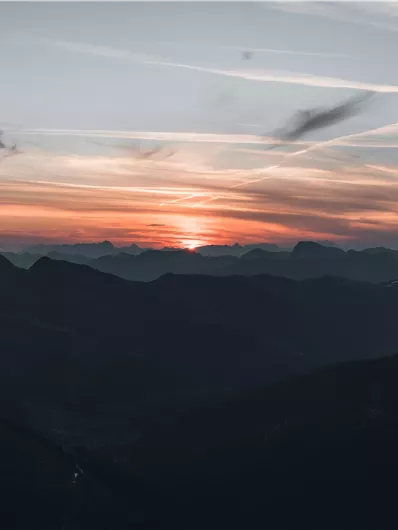 Eine atemberaubende Berglandschaft bei Sonnenuntergang. Der Himmel ist in sanften Farben von Orange und Blau gefärbt.