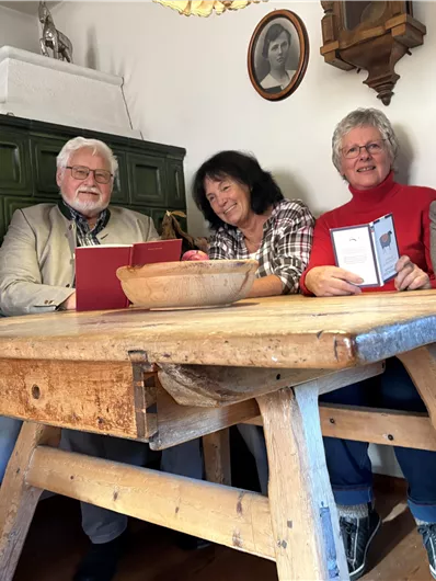 Fünf Personen sitzen an einem Holztisch in einem gemütlichen Raum. Sie scheinen eine angenehme Unterhaltung zu haben und schauen auf ein Tablet.