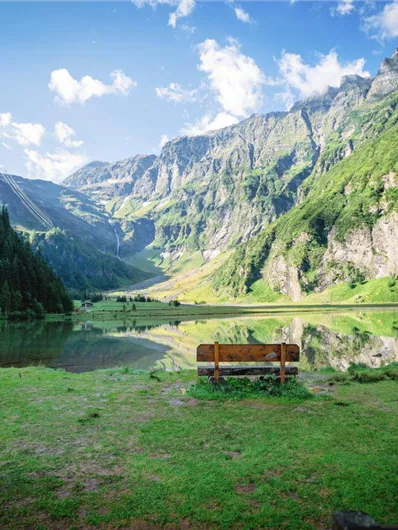 A quiet lake surrounded by majestic mountains and forest. A bench invites you to linger and enjoy the peaceful scenery.