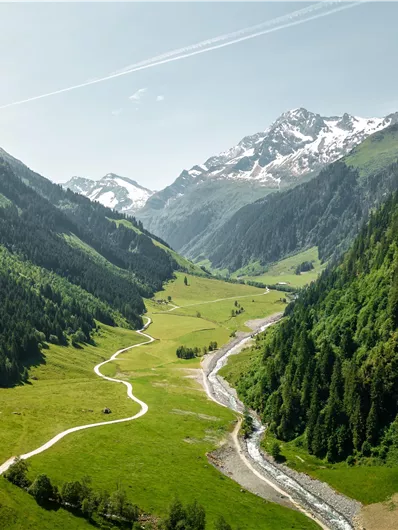 A picturesque alpine valley with green meadows and a clear river. In the background, majestic mountains rise with snow-capped peaks.