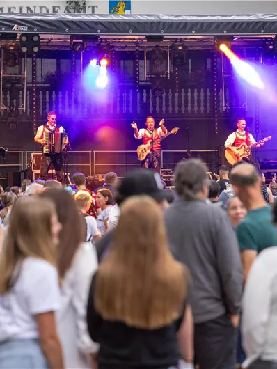 Eine lebhafte Musikveranstaltung mit einer Band auf der Bühne. Viele Zuschauer genießen die Darbietung im Freien.