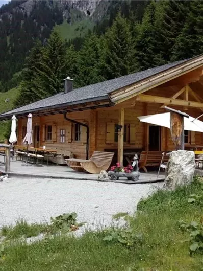 A cozy mountain cabin surrounded by trees and mountains. Outside, there are tables and chairs for guests.