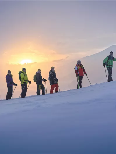 Eine beeindruckende Berglandschaft mit schneebedeckten Gipfeln und Wolken, die das Tal umhüllen. Der Himmel ist klar und strahlend blau.