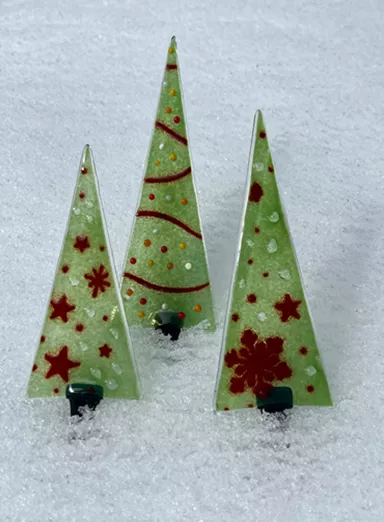 Drie decoratieve kerstbomen van glas staan in de sneeuw. Ze zijn groen met rode patronen en geven een feestelijke sfeer.