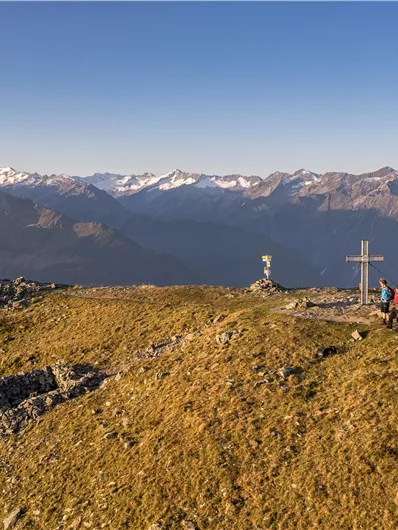 Een vader en zijn zoon zitten op een rots en kijken naar het prachtige berglandschap. Op de achtergrond zijn zachte heuvels en een majestueuze top te zien.