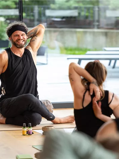 A relaxed yoga session in a bright room with large windows. A teacher demonstrates a stretching exercise while the participants follow attentively.