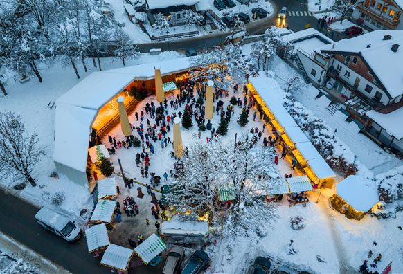 Ein winterlicher Weihnachtsmarkt mit vielen Besuchern in einem verschneiten Dorf. Lichter und Stände schaffen eine festliche Atmosphäre.