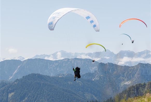 Drei Gleitschirmpiloten fliegen über eine schöne Berglandschaft. Der Himmel ist klar und die Berge sind im Hintergrund sichtbar.