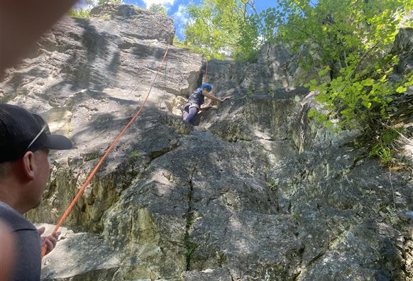 An adult is helping a child climb a rock wall. Both are wearing helmets and appear focused and determined.