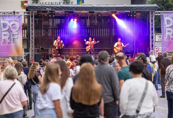Eine lebhafte Musikveranstaltung mit einer Band auf der Bühne. Viele Zuschauer genießen die Darbietung im Freien.