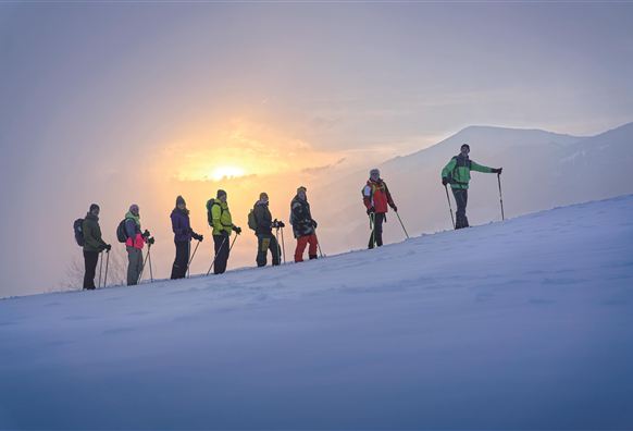 Eine beeindruckende Berglandschaft mit schneebedeckten Gipfeln und Wolken, die das Tal umhüllen. Der Himmel ist klar und strahlend blau.