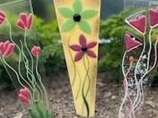 Three colorful plant signs stand in a garden. The signs are decorated with different flower designs and mountains can be seen in the background.