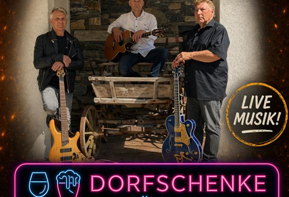 Drei Musiker stehen in einer rustikalen Umgebung mit Akustikgitarren. Sie lächeln und haben Spaß, während im Hintergrund eine Feuerstelle zu sehen ist.
