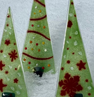 Drie decoratieve kerstbomen van glas staan in de sneeuw. Ze zijn groen met rode patronen en geven een feestelijke sfeer.