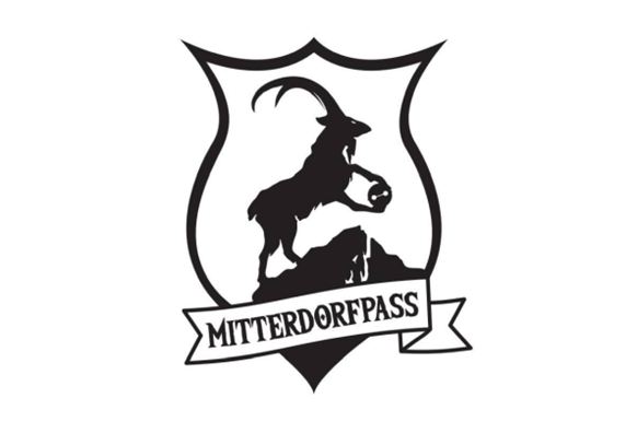 A stylized coat of arms featuring a goat figure standing on a rock. Beneath it is the inscription "MITTERDORFPASS".
