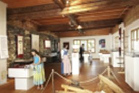 A bright room with a wooden floor and a wooden ceiling. On the walls, bookshelves and exhibition objects are visible.