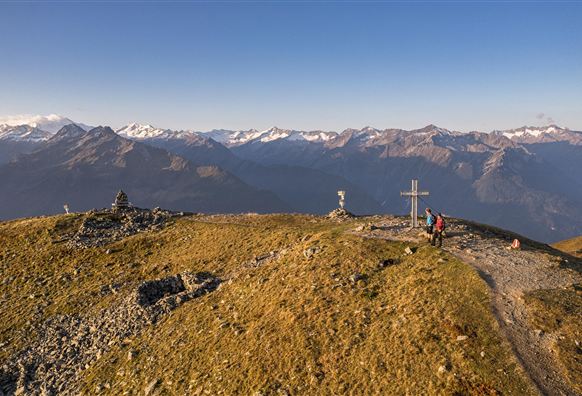 Een vader en zijn zoon zitten op een rots en kijken naar het prachtige berglandschap. Op de achtergrond zijn zachte heuvels en een majestueuze top te zien.
