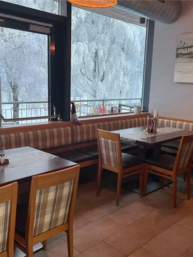 Een gezellig restaurant met houten tafels en stoelen. De grote ramen bieden uitzicht op een besneeuwd landschap.