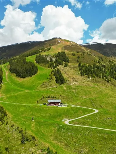 A green mountain landscape with gentle hills and a small wooden house. The sky is partly cloudy with a few white clouds.