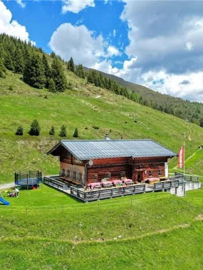 A cozy cabin in the midst of green meadows and mountains. The surroundings are peaceful with a playground and blue sky.