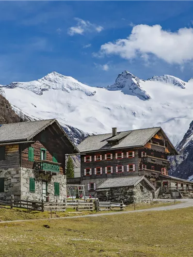 A picturesque mountain landscape with traditional wooden houses. In the background, majestic mountains and a blue sky can be seen.