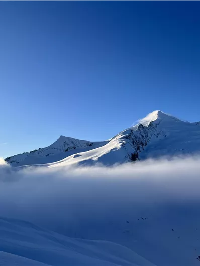 A breathtaking winter landscape with snow-covered mountains and clear blue sky. Gentle mists give the scene a mystical atmosphere.