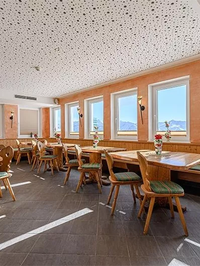 An inviting restaurant with wooden tables and chairs. Large windows offer a view of the mountains and provide plenty of daylight.