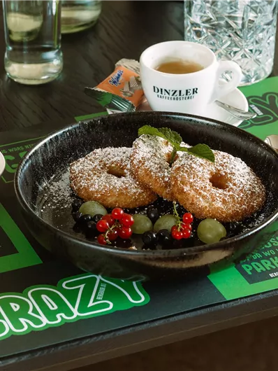 A delicious dessert with two donuts, decorated with powdered sugar and fresh berries, on a black plate. Accompanied by a scoop of vanilla ice cream and a cup of coffee.
