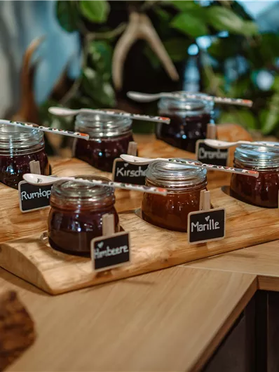 A rustic table with several jars of jam and Nutella. The jars are labeled and placed on a wooden board.