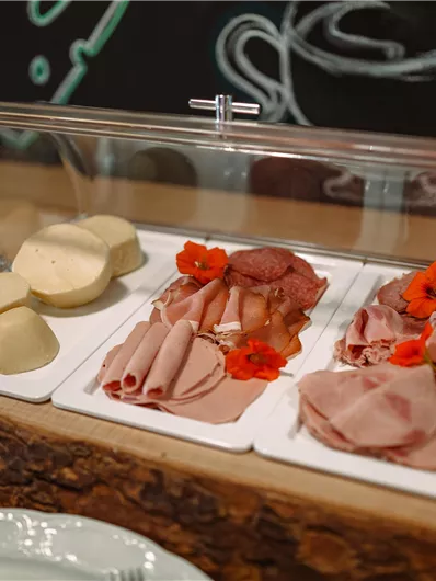 A selection of cold cuts and cheese on a wooden board. The platters are decorated with edible flowers.
