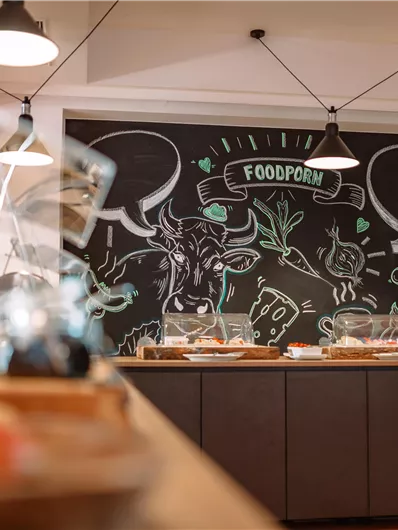A modern kitchen with a large chalkboard decorated with colorful food drawings. Various dishes are ready on the table.