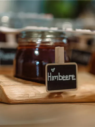 A selection of jam jars on a wooden board. The labels show the varieties, including raspberry and apricot.