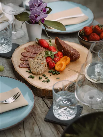 A beautifully set table with a rustic wooden board. On it are meats, fresh strawberries, and other snacks.