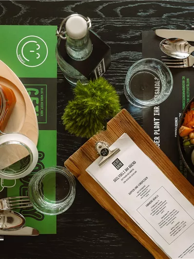 A elegantly set table with a colorful dish, water bottles, and a menu. The surroundings are modern and inviting.