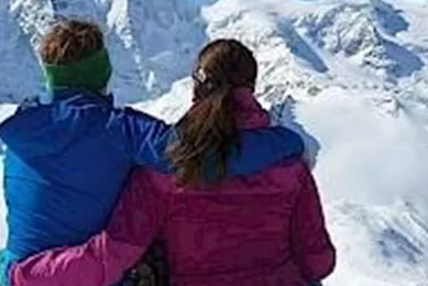 Een paar zit op een rots en geniet van het uitzicht op besneeuwde bergen. De lucht is helder en blauw.