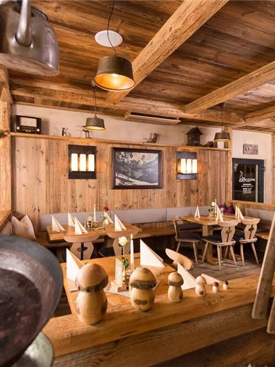Eine gemütliche, rustikale Gaststätte mit Holzwänden und warmem Licht. Tische sind für Gäste gedeckt und traditionelle Dekoration ist sichtbar.
