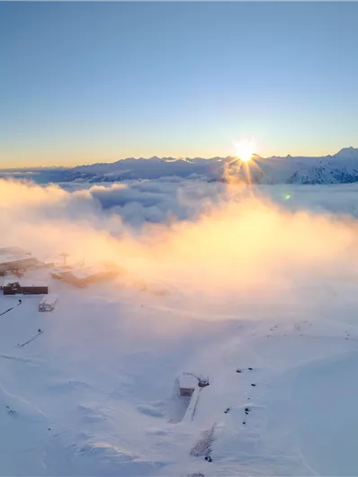 An impressive winter landscape with snow-covered mountains and a beautiful sunrise. Soft clouds drift over the snow-covered terrain.