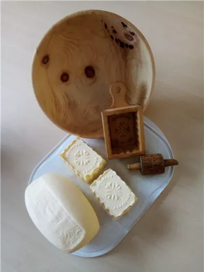 A wooden bowl with various shapes of cheese and a wooden stamp. The cheeses are decorative and handmade.