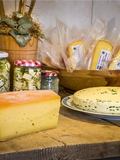 Eine Auswahl an verschiedenen Käsesorten auf einem Holztisch. Im Hintergrund sind eingelegte Käse und Verpackungen sichtbar.