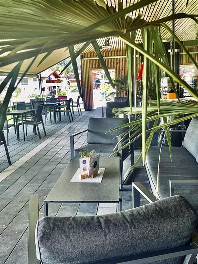 Een stijlvol café met comfortabele zitplaatsen en een uitnodigende sfeer. Op de achtergrond zijn tafels en stoelen buiten te zien.