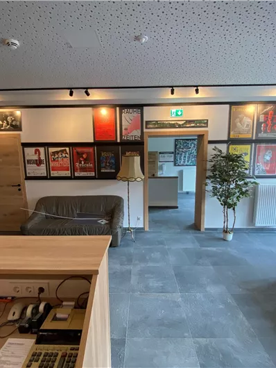 Ein einladendes Foyer mit verschiedenen Plakaten an der Wand. Es gibt einen Couchbereich und Pflanzen, die zur gemütlichen Atmosphäre beitragen.