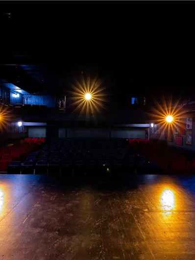 Eine leere Theaterbühne mit schummriger Beleuchtung. Im Hintergrund sind Reihen von leeren Sitzen sichtbar.