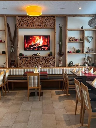 Een gezellig restaurant met houten planken en rustieke decoratie. De tafels zijn voor gasten gedekt, en een flikkerend haardvuur wordt op een scherm weergegeven.
