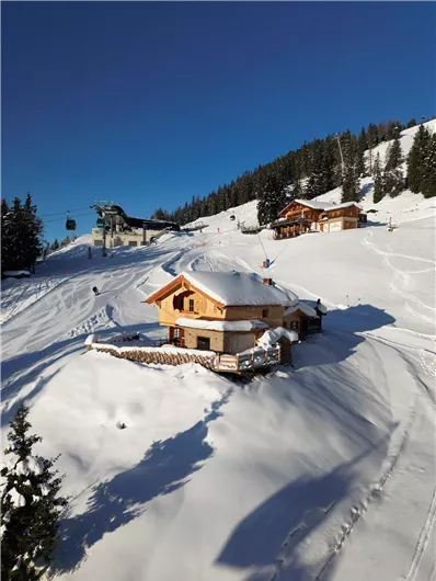 Eine verschneite Berglandschaft mit gemütlichen Hütten. Der Himmel ist klar und blau, und Ski- und Snowboardfahrer sind unterwegs.