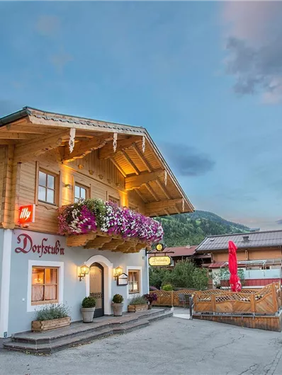 Ein traditionelles alpenländisches Gasthaus mit blühenden Balkonblumen. Der Abendhimmel zeigt sanfte Farben über der ruhigen Straße.