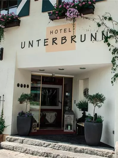 An inviting hotel named Unterbrunn with a lovely entrance area. Flowers decorate the windows and surroundings.