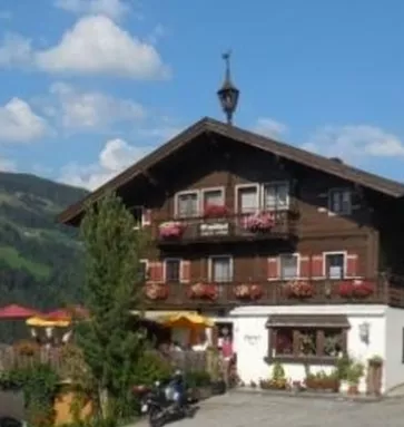 Een charmant, twee verdiepingen tellend houten huis met balkons en kleurrijke bloembakken. Op de achtergrond zijn idylische bergen en een blauwe lucht te zien.