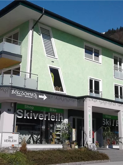 Ein modernes Gebäude mit einer grünen Fassade und großen Fenstern. Im Erdgeschoss befindet sich ein Skiverleih.