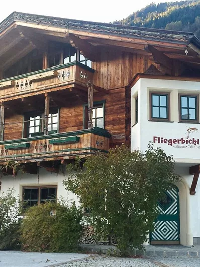A traditional alpine hut with a wooden façade and several balconies. Surrounded by trees and mountains, it radiates rural charm.